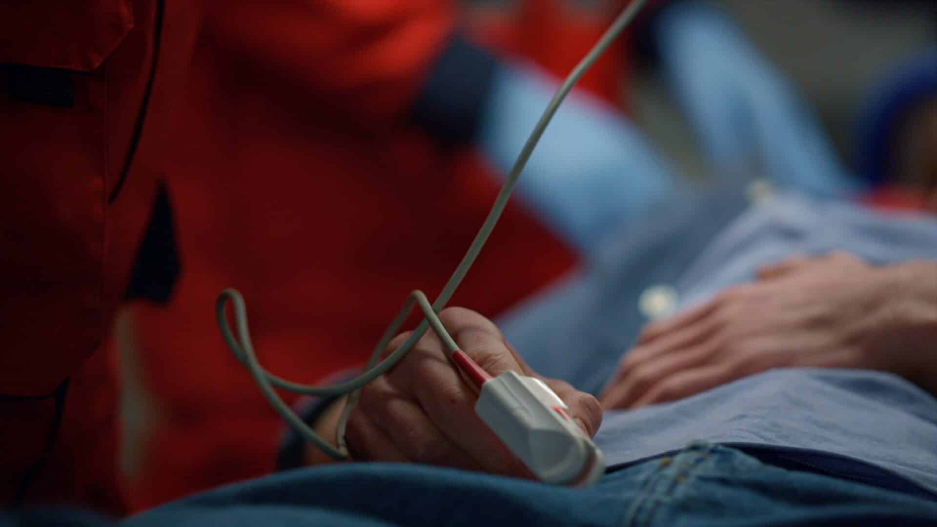 Uma pessoa deitada segura um sensor médico preso ao dedo, usado para monitorar sinais vitais em um ambiente hospitalar.