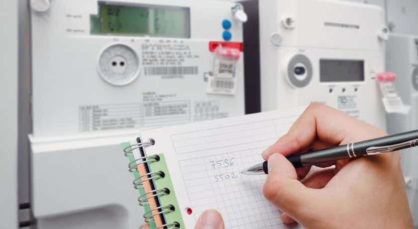 Um medidor de energia e uma pessoa anotando em um bloco